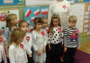 Grupa dzieci ze swoją panią śpiewa hymn Polski